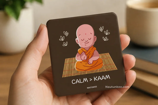A hand holds a fridge magnet featuring a cartoon illustration of a meditating monk in orange robes with the text CALM > KAAM Nautunkee